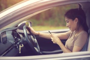 A young driver is looking at her phone instead of looking at the road while she is at the wheel.