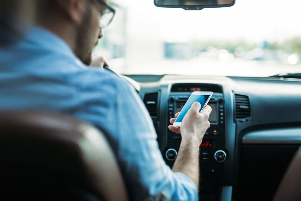 man in blue shirt and glasses in car texting while driving